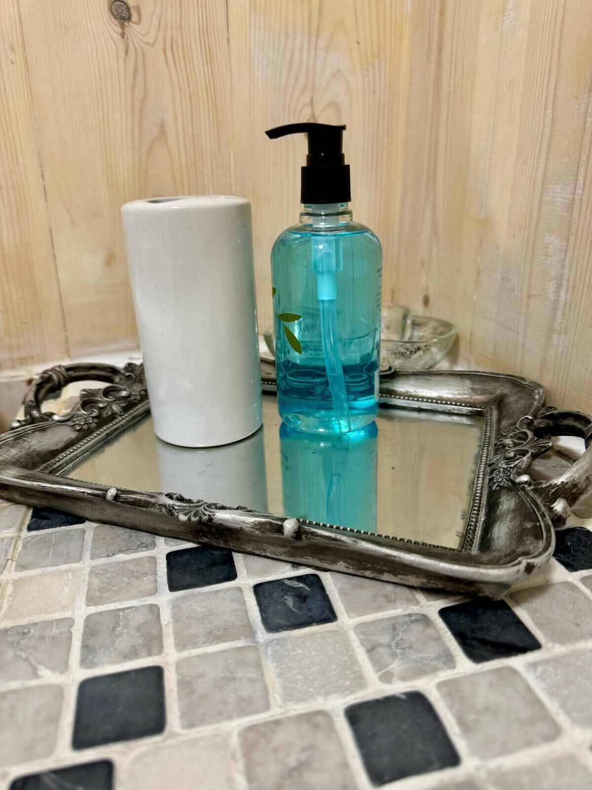 A bathroom vanity with a white soap dispenser and a blue liquid soap bottle on a glass tray with an ornate metal frame.