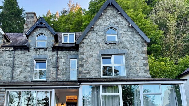 A stone building with a dark entrance, multiple windows, and a sign for Fairhaven Stay. - Fairhaven Stay (Betws-Y-Coed)