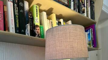 Una lámpara con base de elefante sobre una mesa blanca, una estantería con varios libros y una pared blanca al fondo.