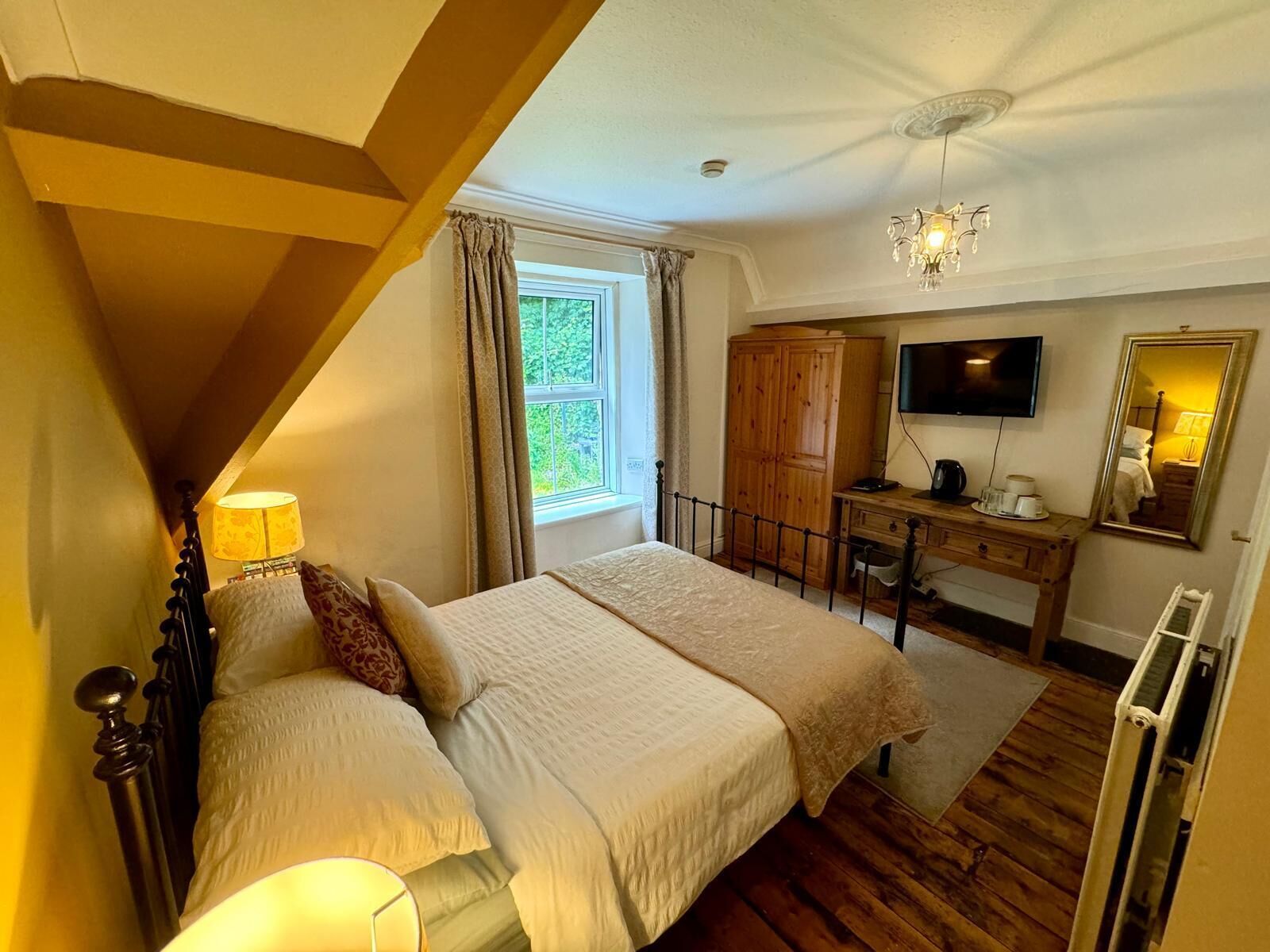 A bedroom with a bed, bedside tables, a wardrobe, a desk, a television, and a mirror.