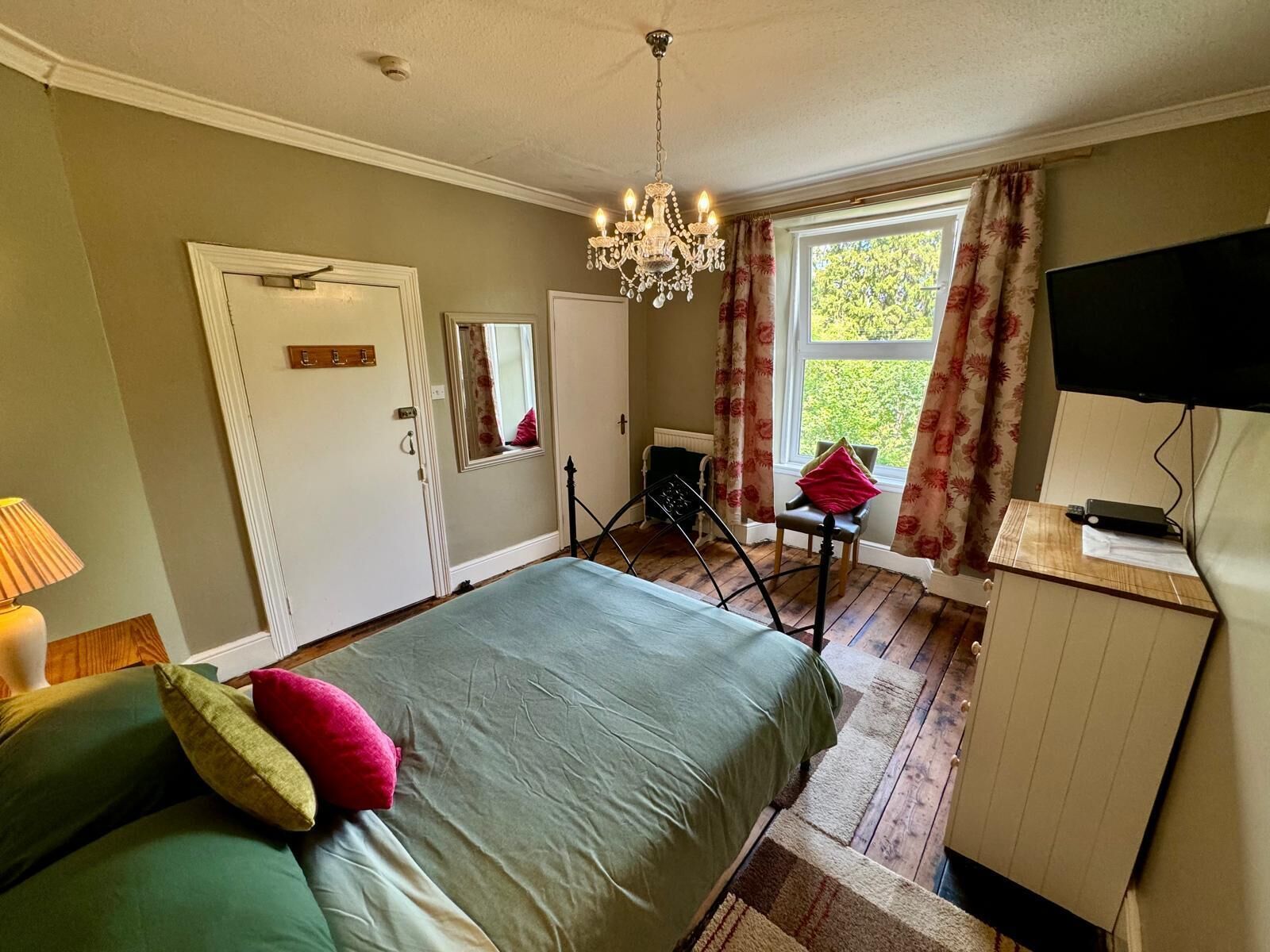 A bedroom with a bed, a desk, a chair, a television, and a window with curtains.