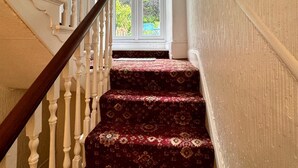 A staircase with a wooden handrail and white balusters, leading to a room with a large window and a view of greenery outside. - Fairhaven Stay (Betws-Y-Coed)