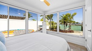 A bedroom with a large bed, a ceiling fan, and a view of a pool and palm trees.