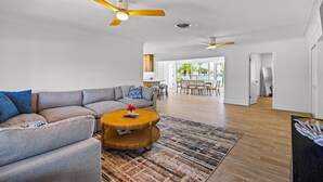 A spacious living area with a large sofa, a round coffee table, and a dining table in the background.