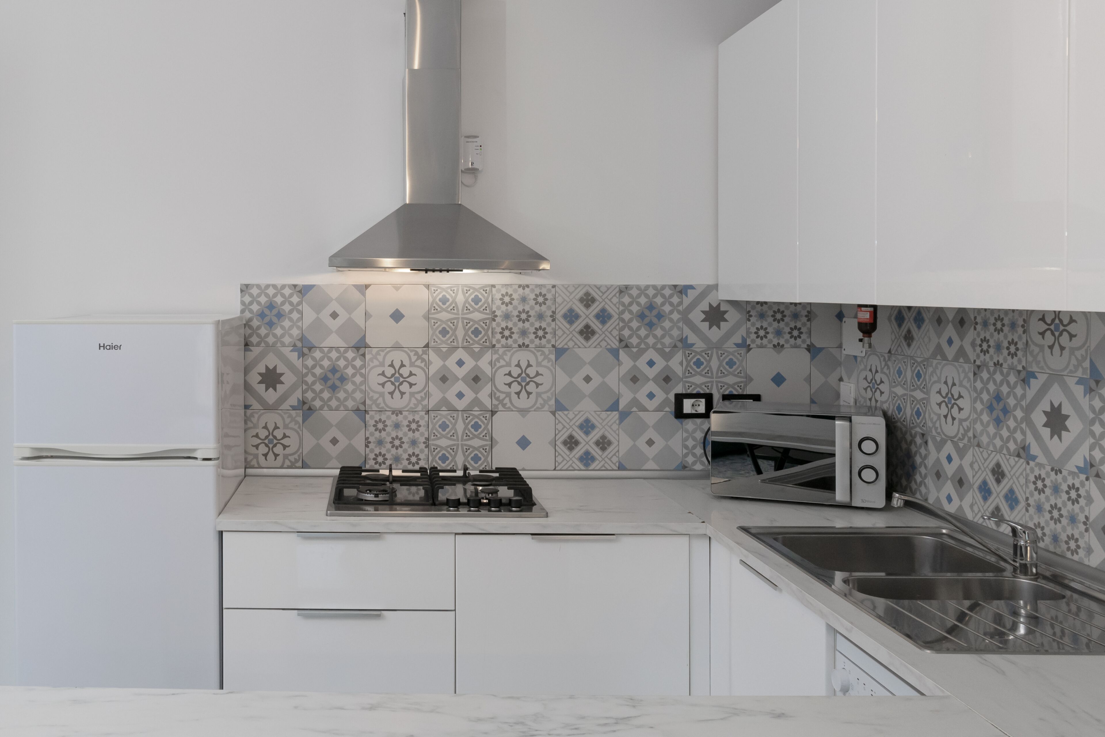 A modern kitchen with white cabinets, a gas stove, a built-in oven, and a stainless steel sink.