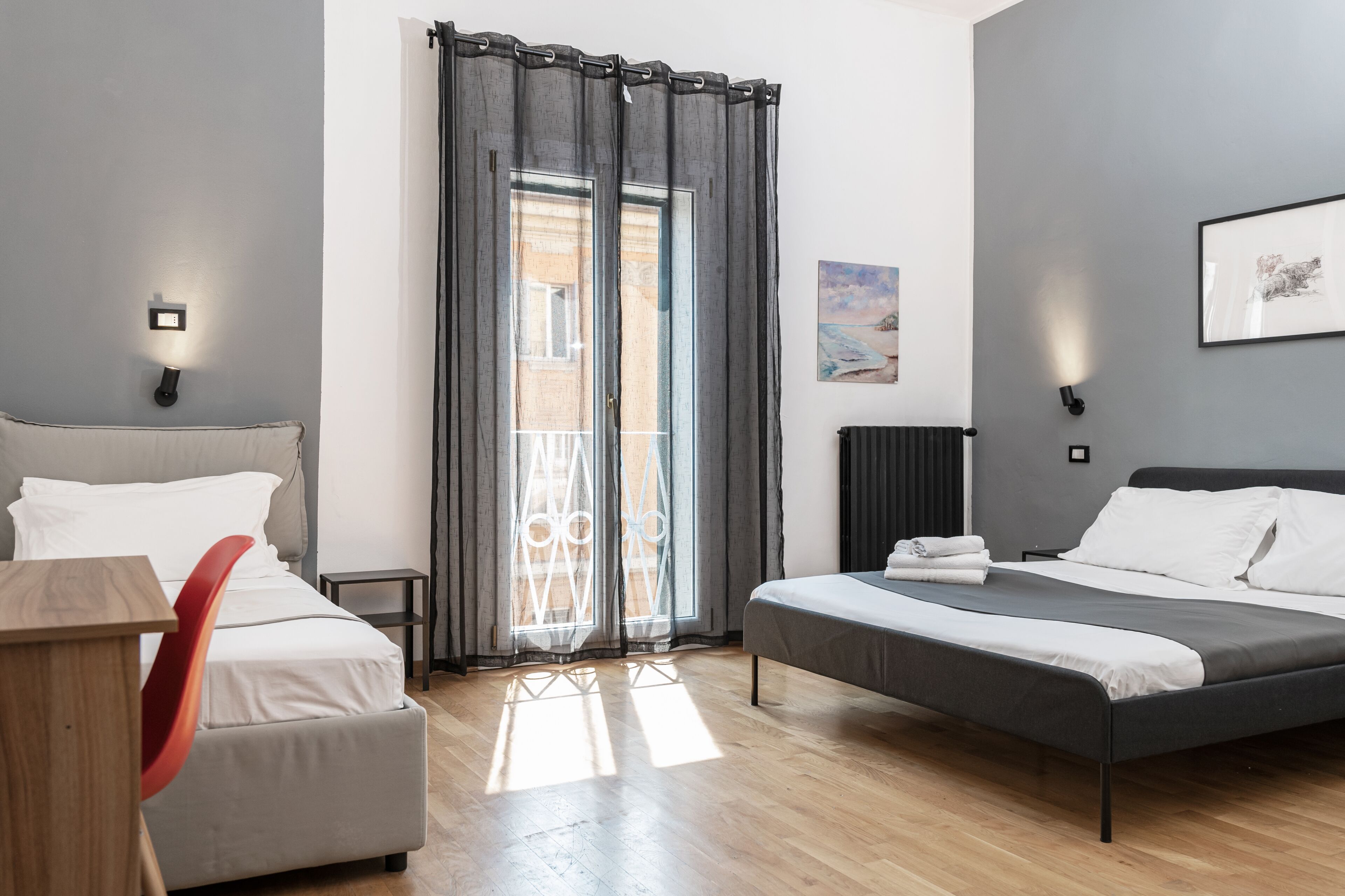 A modern bedroom with a bed, a chair, a table, and a view of the outside through a window with curtains.