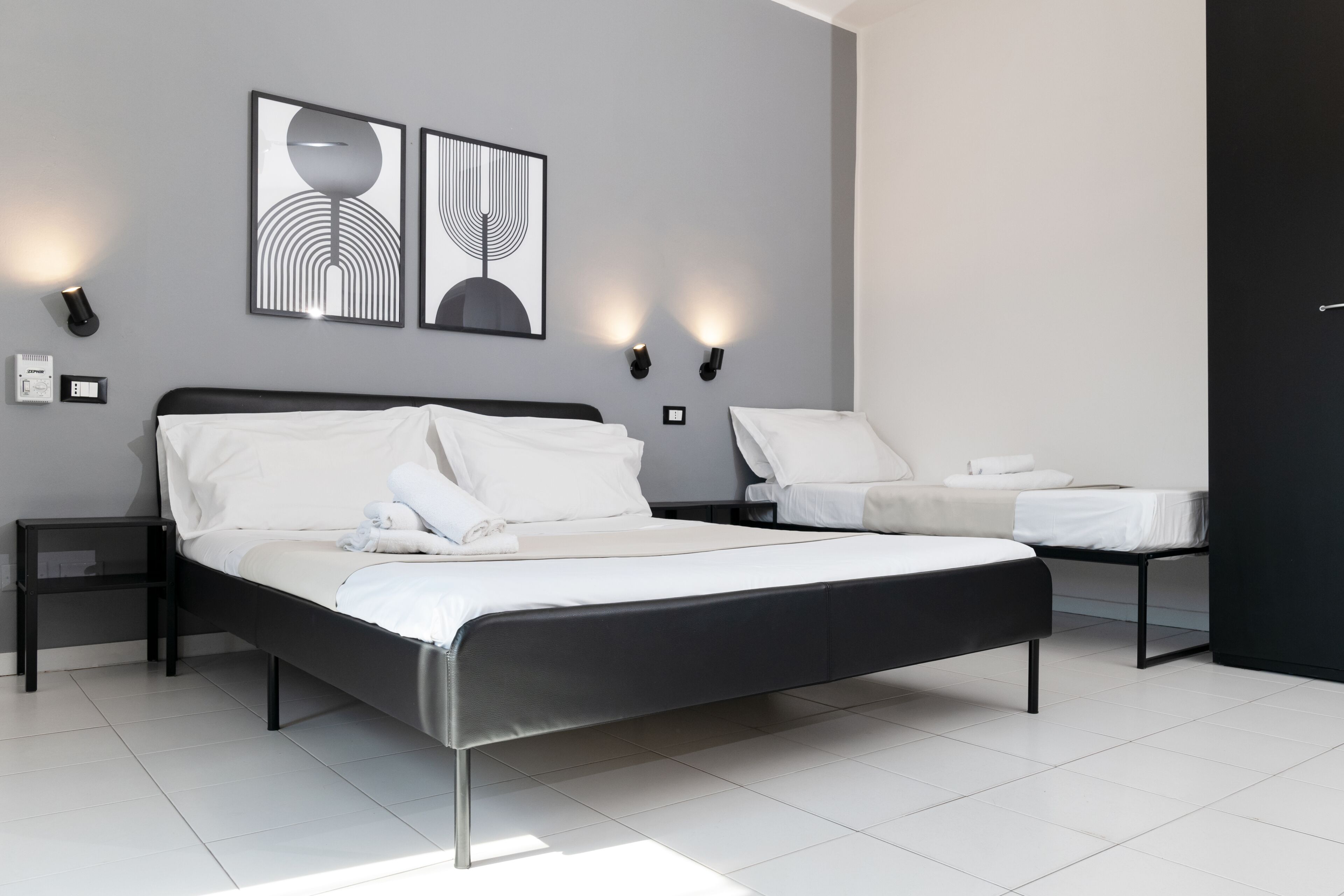 Une chambre moderne avec un grand lit, des tables de chevet, des lampes fixées au mur et des œuvres d’art abstraites.
