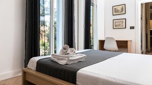 A neatly made bed with rolled towels, a desk with a chair, and two framed pictures on the wall. - Saragozza Apartments (Bologna)