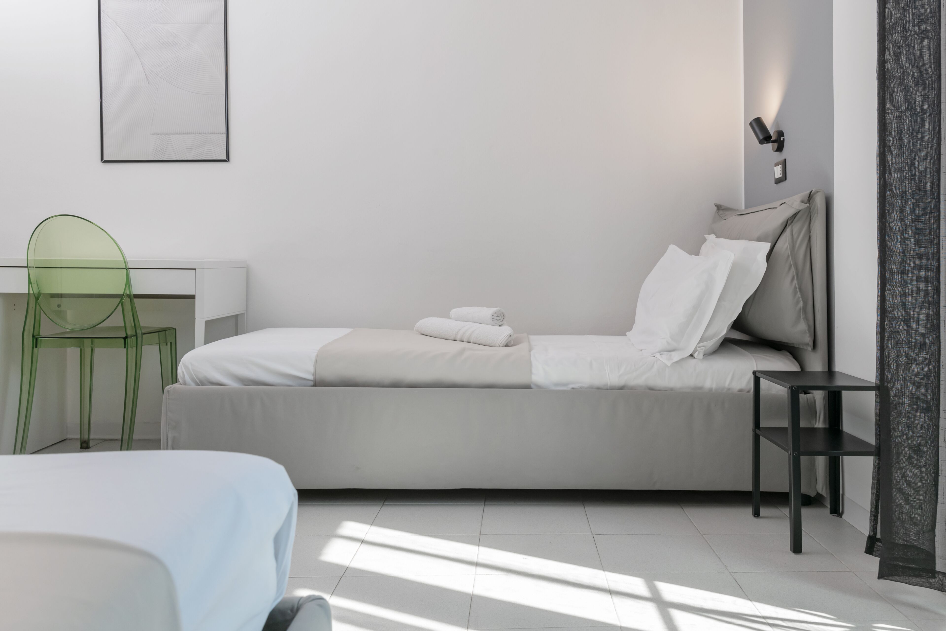 A modern bedroom with a bed, a desk, a chair, and a bedside table.
