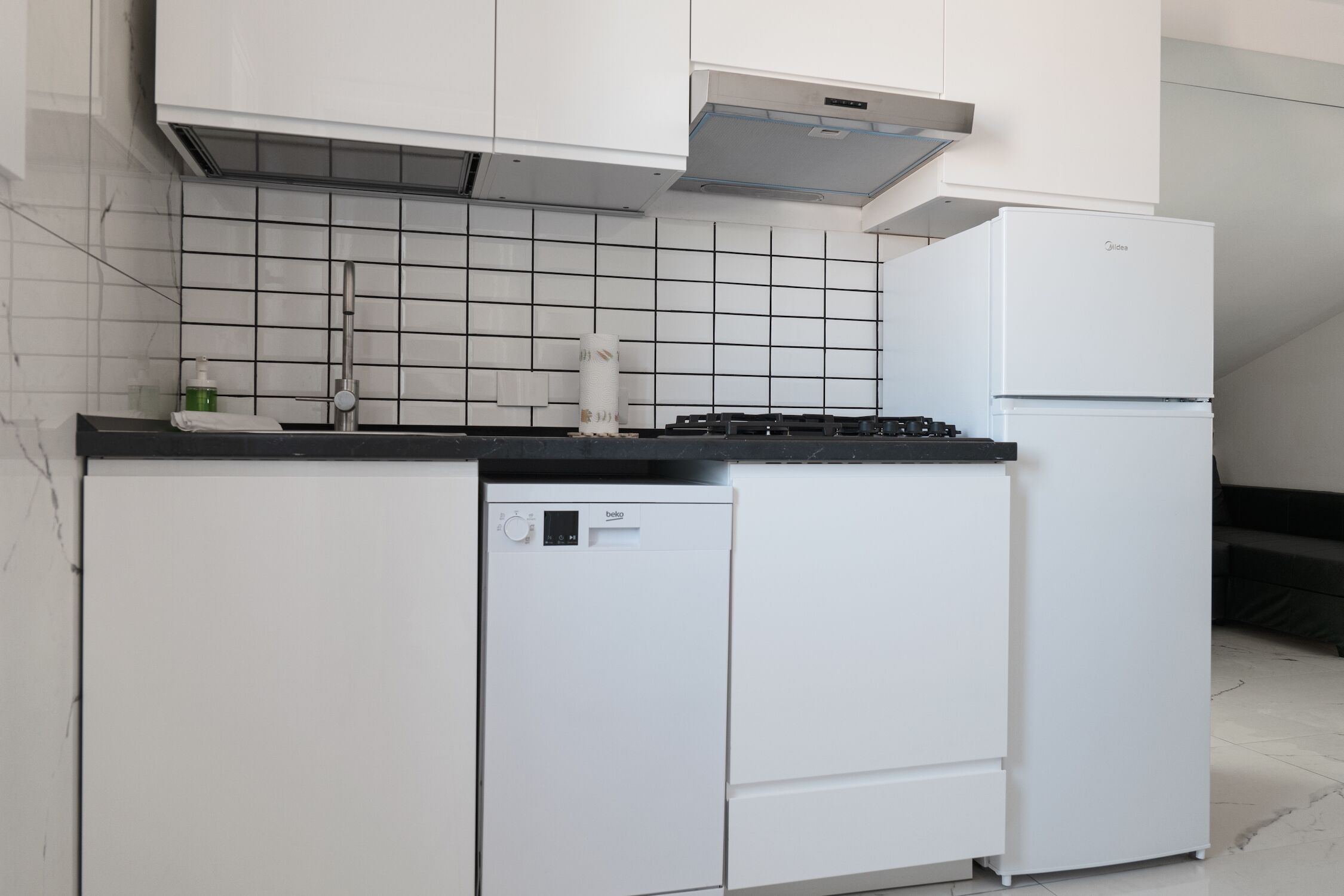 Een moderne keuken met witte kasten, een zwart aanrecht, een geïntegreerde vaatwasser en een witte koelkast.
