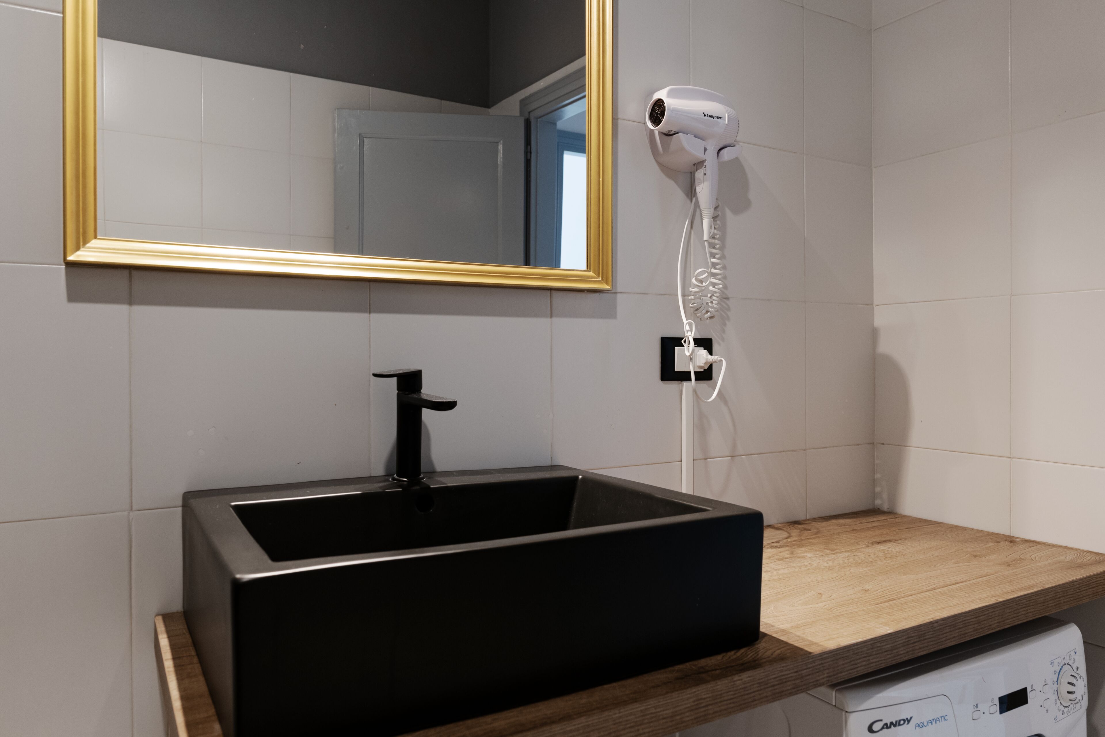 A bathroom with a black sink, a gold-framed mirror, and a hairdryer mounted on the wall.