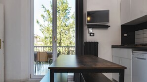 A modern kitchen with a large table, a TV mounted above the counter, and a view of the outside through a glass door. - Saragozza Apartments (Bologna)