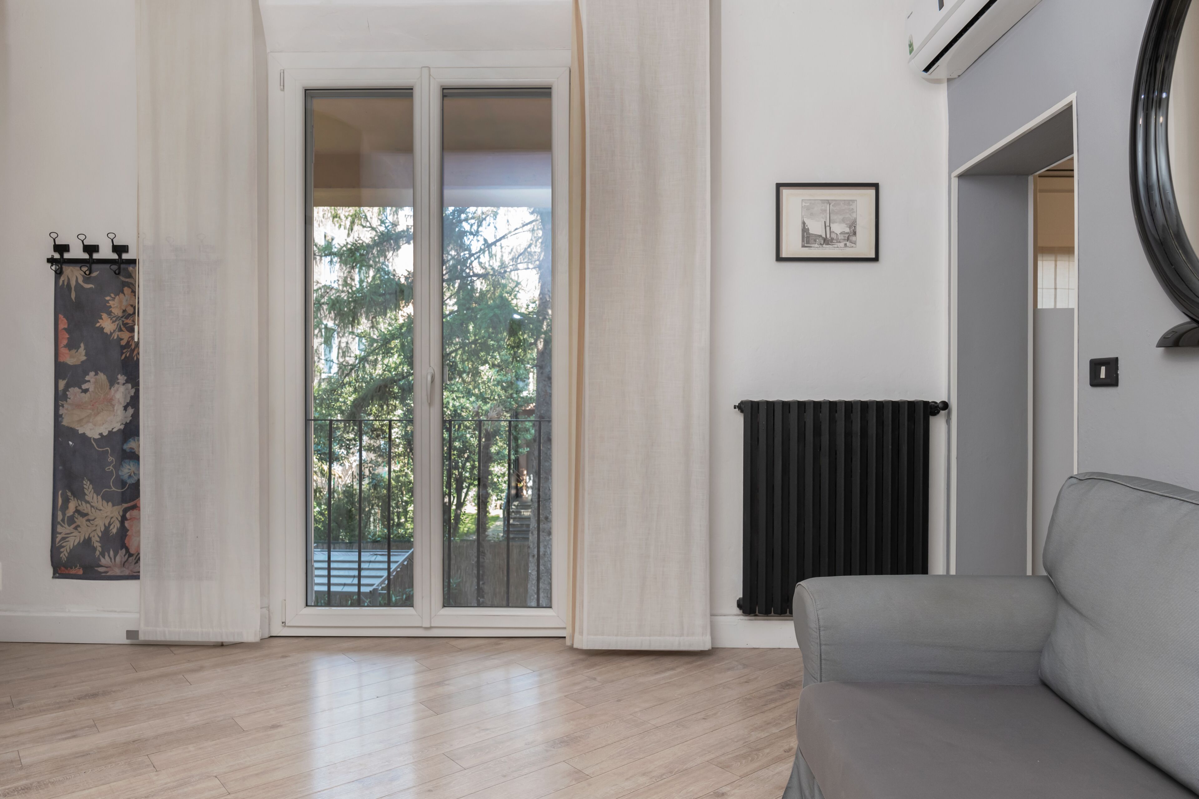A room with a sliding glass door, a radiator, a grey sofa, and a framed picture on the wall.
