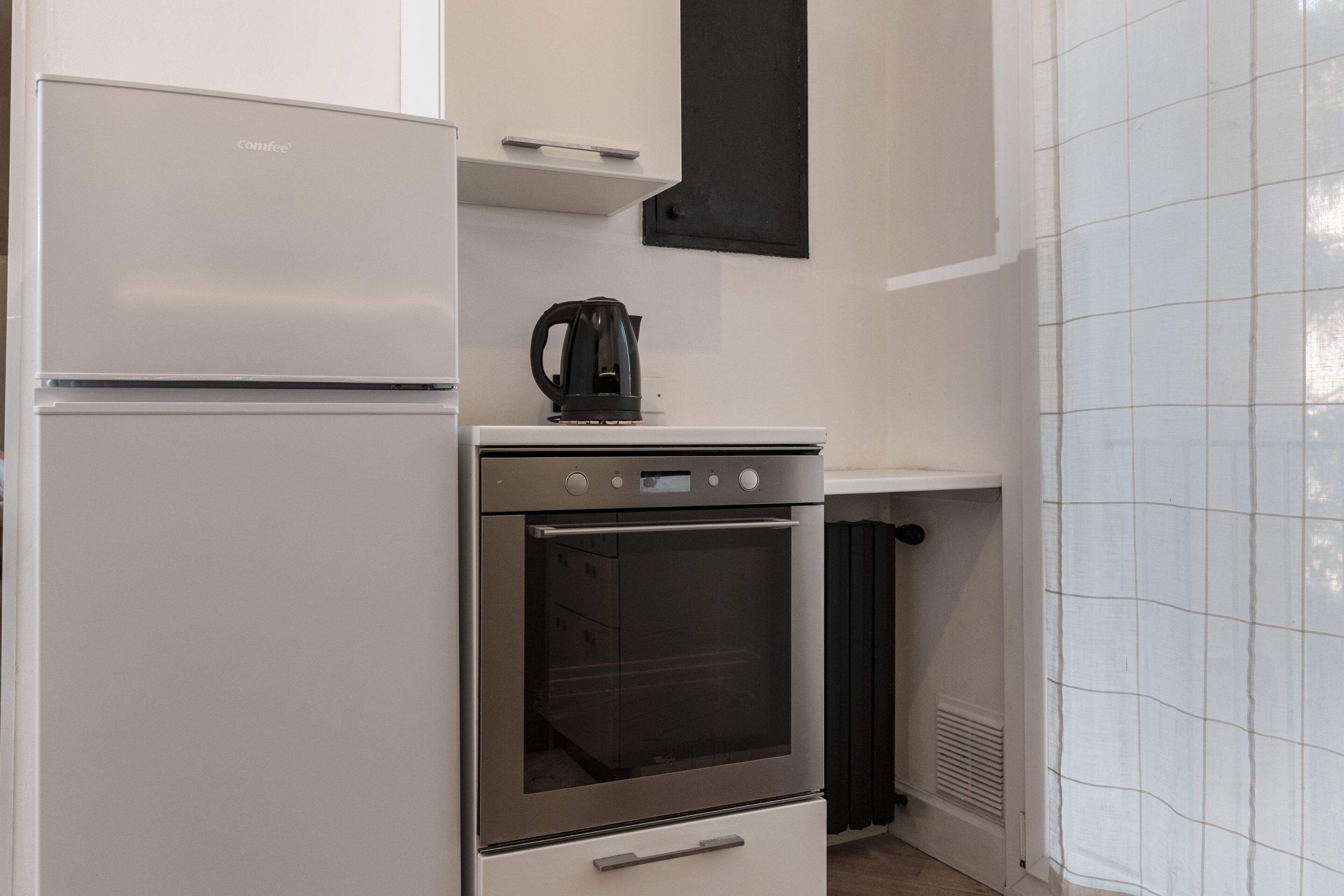 Une cuisine compacte équipée d’un réfrigérateur, d’un four et d’une machine à café posée sur le plan de travail.