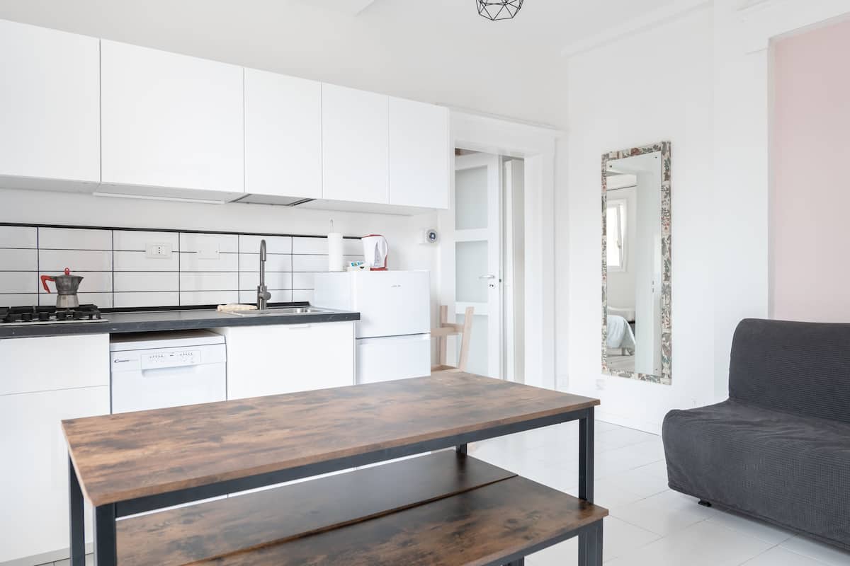 A modern kitchen with white cabinets, a wooden table, and a grey sofa.