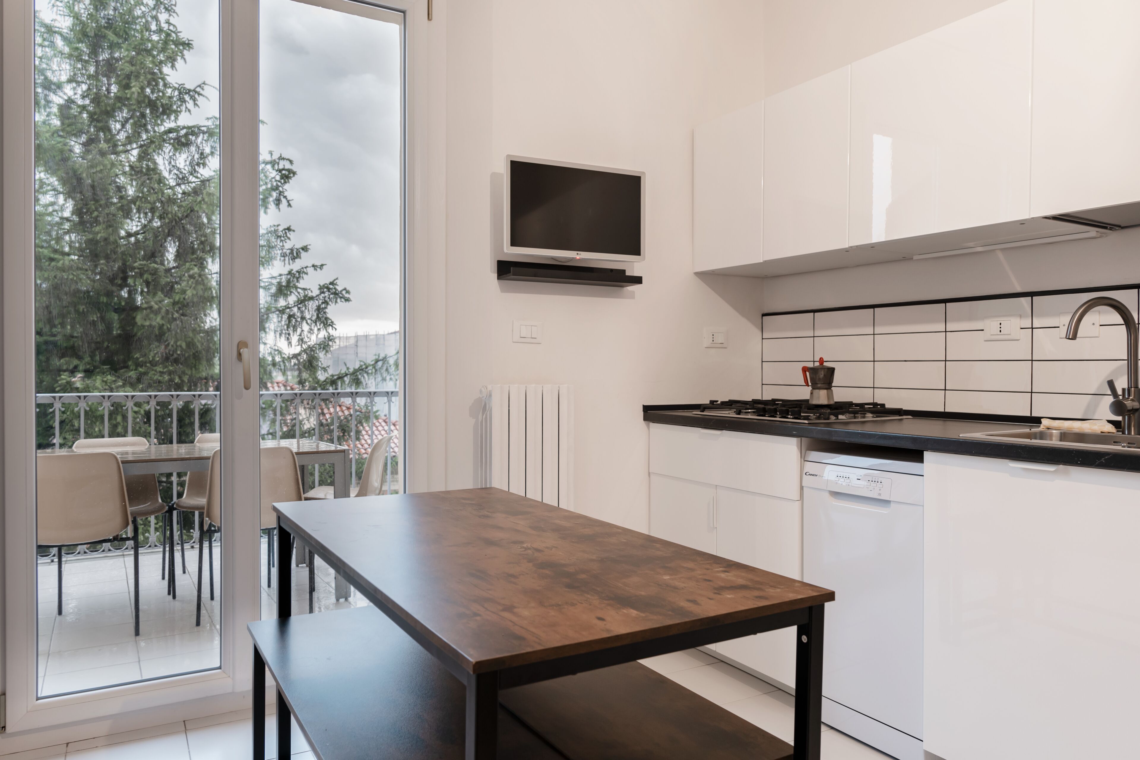 Une cuisine moderne avec un coin repas, un téléviseur fixé au-dessus du comptoir et une vue sur l’extérieur.