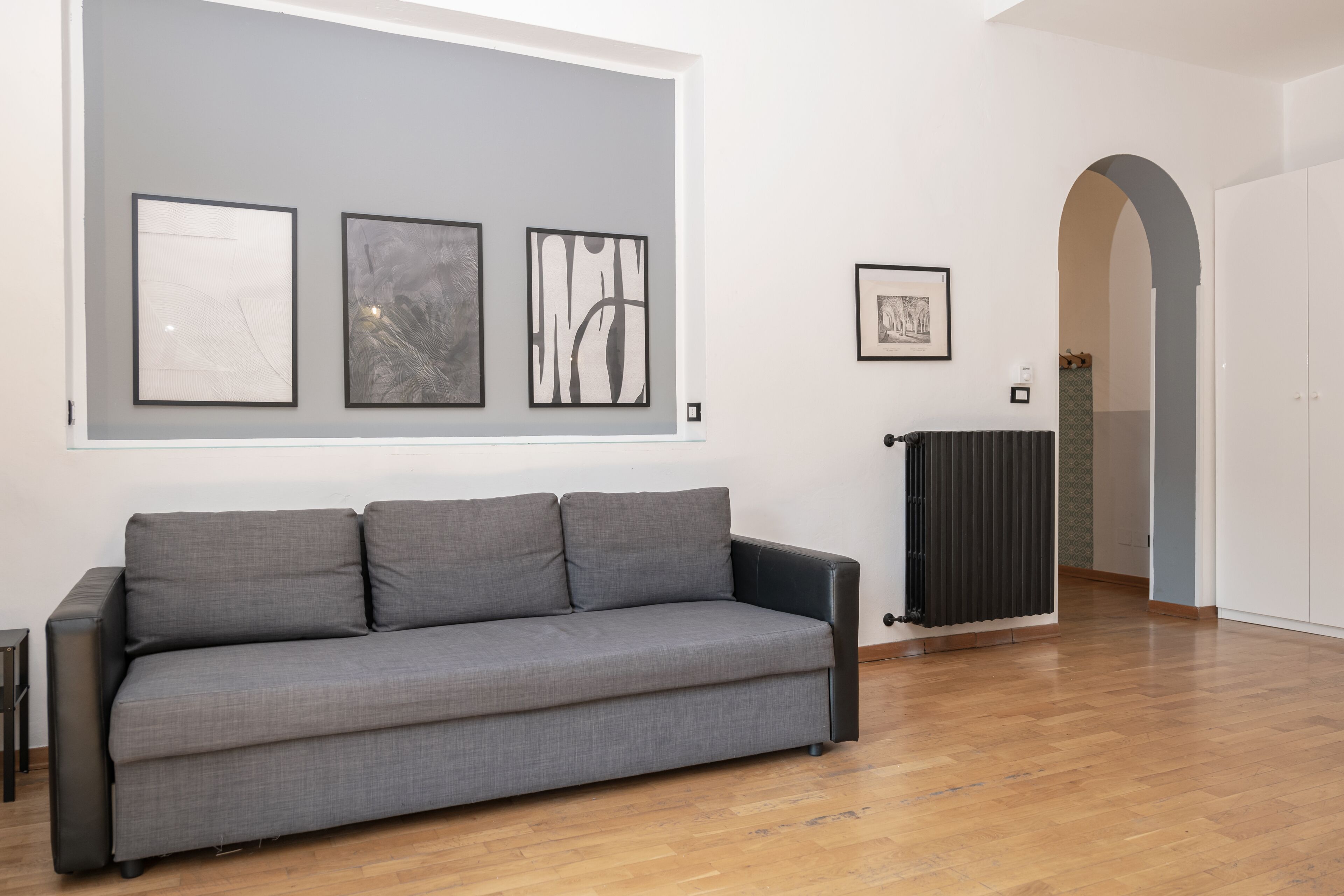 A modern living room with a grey sofa, a radiator, and framed artwork on the wall.