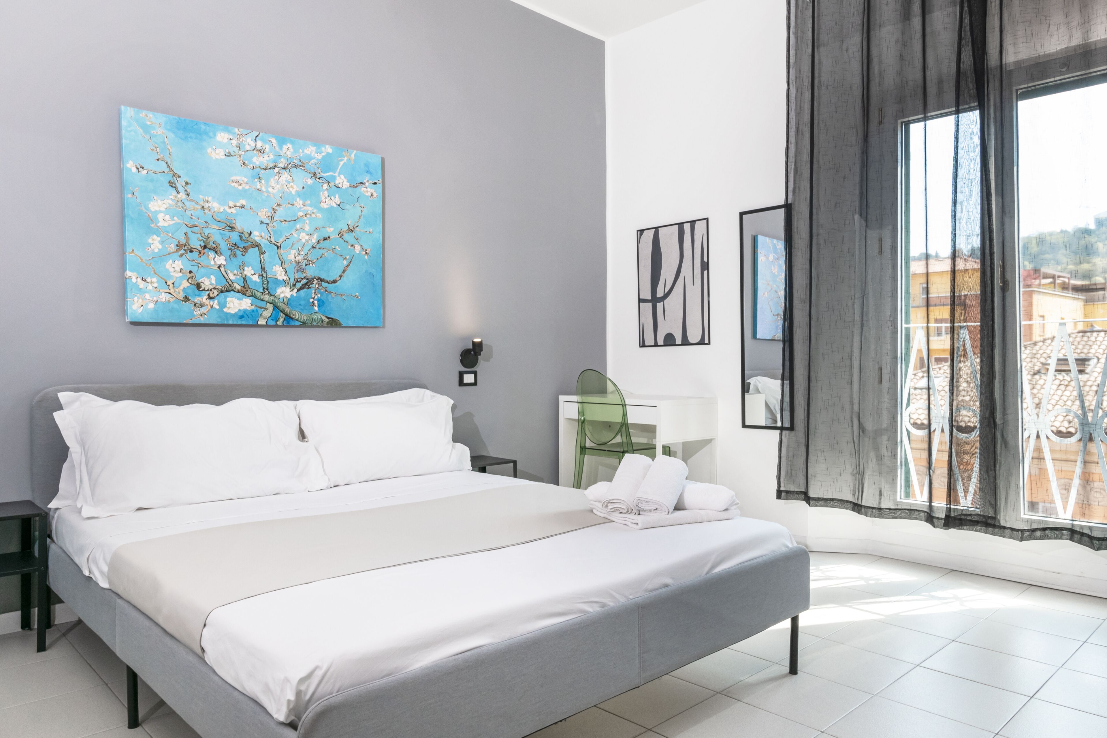 A modern bedroom with a large bed, a painting of a tree, a window with a view, and a bedside table.