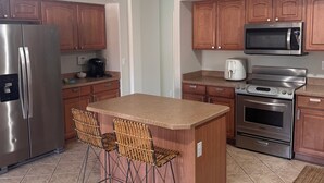 A modern kitchen with a central island, stainless steel appliances, wooden cabinets, and a tiled floor.