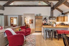 Un amplio espacio de sala con un sofá rojo, una mesa de comedor de madera con taburetes, y una cocina con armarios de madera y una campana extractora de acero inoxidable.