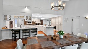 A modern kitchen with white cabinetry, a central island with bar stools, and a dining area with a wooden table and chairs. - Secluded Luxe 5BR Estate Pool, Wineries, Near ND (Niles)