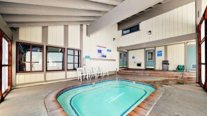 Une piscine intérieure dont les bords sont recouverts de carrelage, entourée d’une terrasse en bois. On y trouve des chaises longues et un panneau d’avertissement sur le mur.