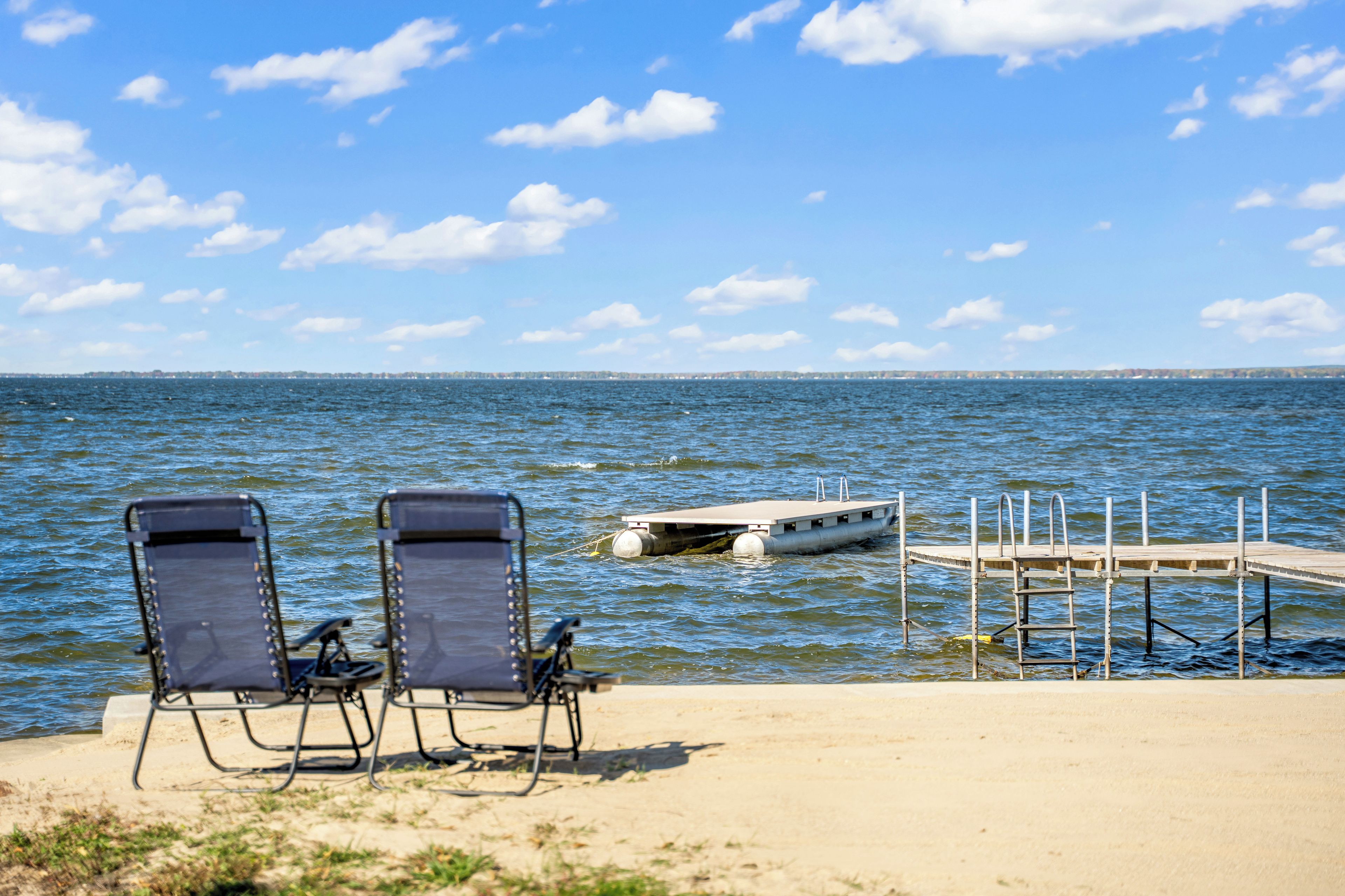 Two beach chairs facing a calm sea with a dock and a boat.