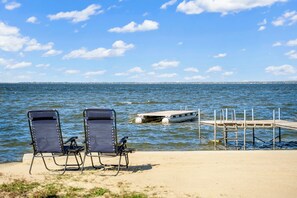 Two beach chairs facing a calm sea with a dock and a boat.