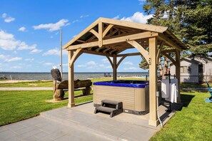 A wooden gazebo with a hot tub, a wooden bench, and a view of the water.