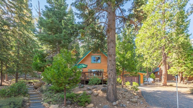 A cabin with a wooden deck, surrounded by trees and a stone pathway leading to the entrance.