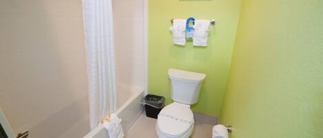 A bathroom with a toilet, a bathtub, a shower curtain, a trash bin, and a towel rack with towels.