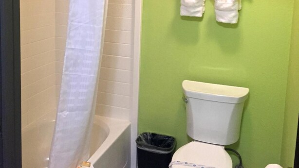 Ein Badezimmer mit grüner Wand, einer weißen Toilette, einer Dusche mit weißem Vorhang und zwei weißen Handtüchern an einem Halter.