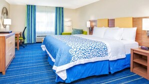 Ein Hotelzimmer mit einem großen Bett, einem Schreibtisch, einem Stuhl und einem mit Vorhängen versehenen Fenster.