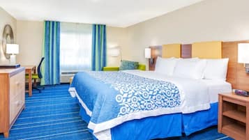 A hotel room with a large bed, a desk, a chair, and a window with curtains.