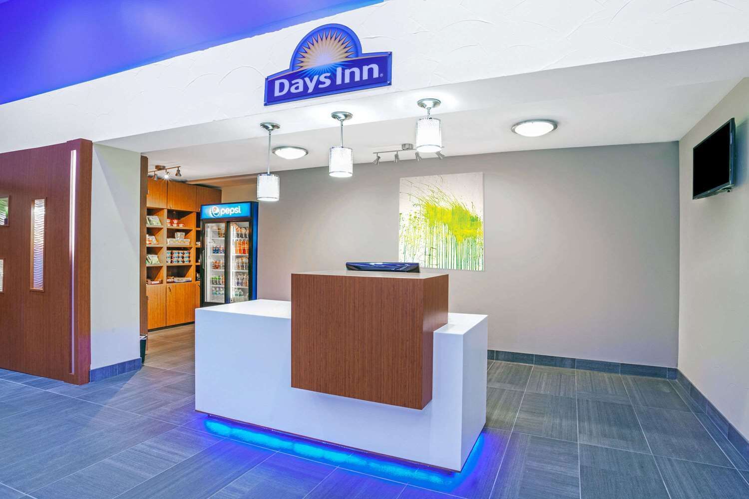 A reception desk with a 'Days Inn' sign above, a Pepsi refrigerator, and a wall with a vertical bamboo-like artwork.