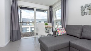 A modern living room with a grey sofa, a colorful pillow, and a dining area with a white table and chairs. - Pet-friendly With Balcony and Shared Garden (London)