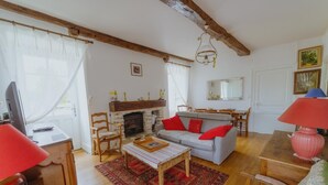 A cozy living room with a fireplace, a sofa with red cushions, a wooden coffee table, and a dining area with a table and chairs. - La Maison de Yette - CHEILLY-LES-MARANGES (CHEILLY-LES-MARANGES)