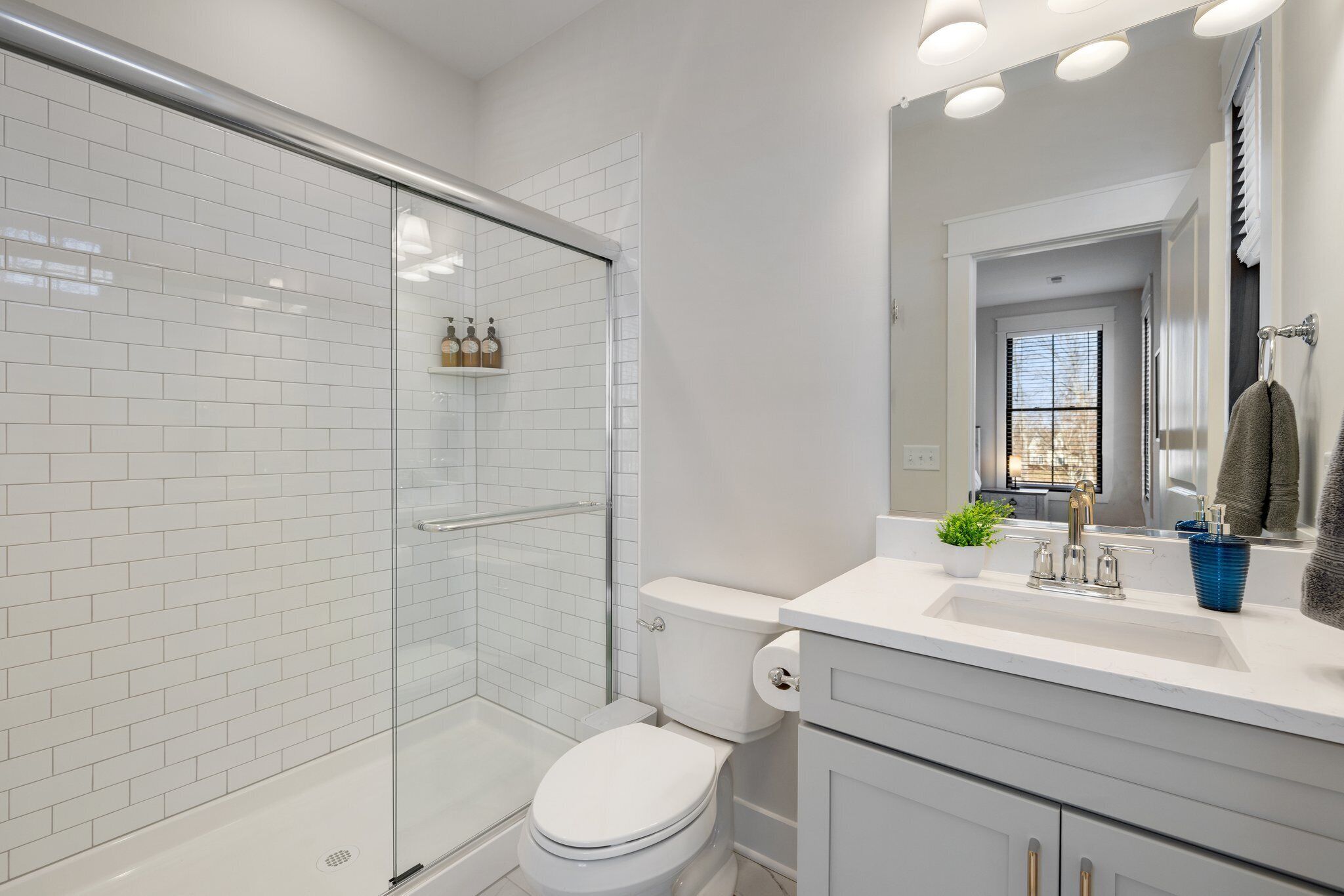 Une salle de bain moderne avec une douche à parois de verre, des toilettes blanches et un lavabo avec un miroir au-dessus.