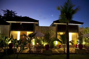 A building with a covered outdoor seating area, potted plants, and a palm tree. - Muaya Villa (Bali)