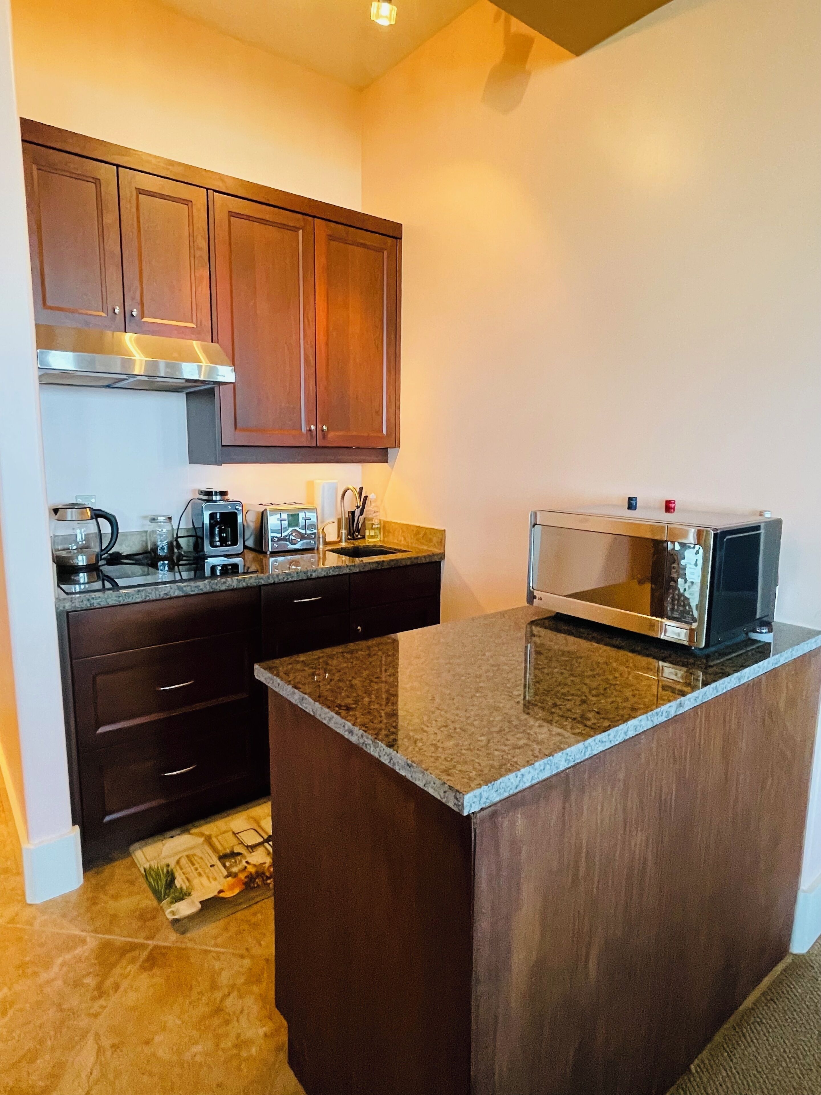 A compact kitchen with dark wooden cabinets, a granite countertop, and a built-in microwave.