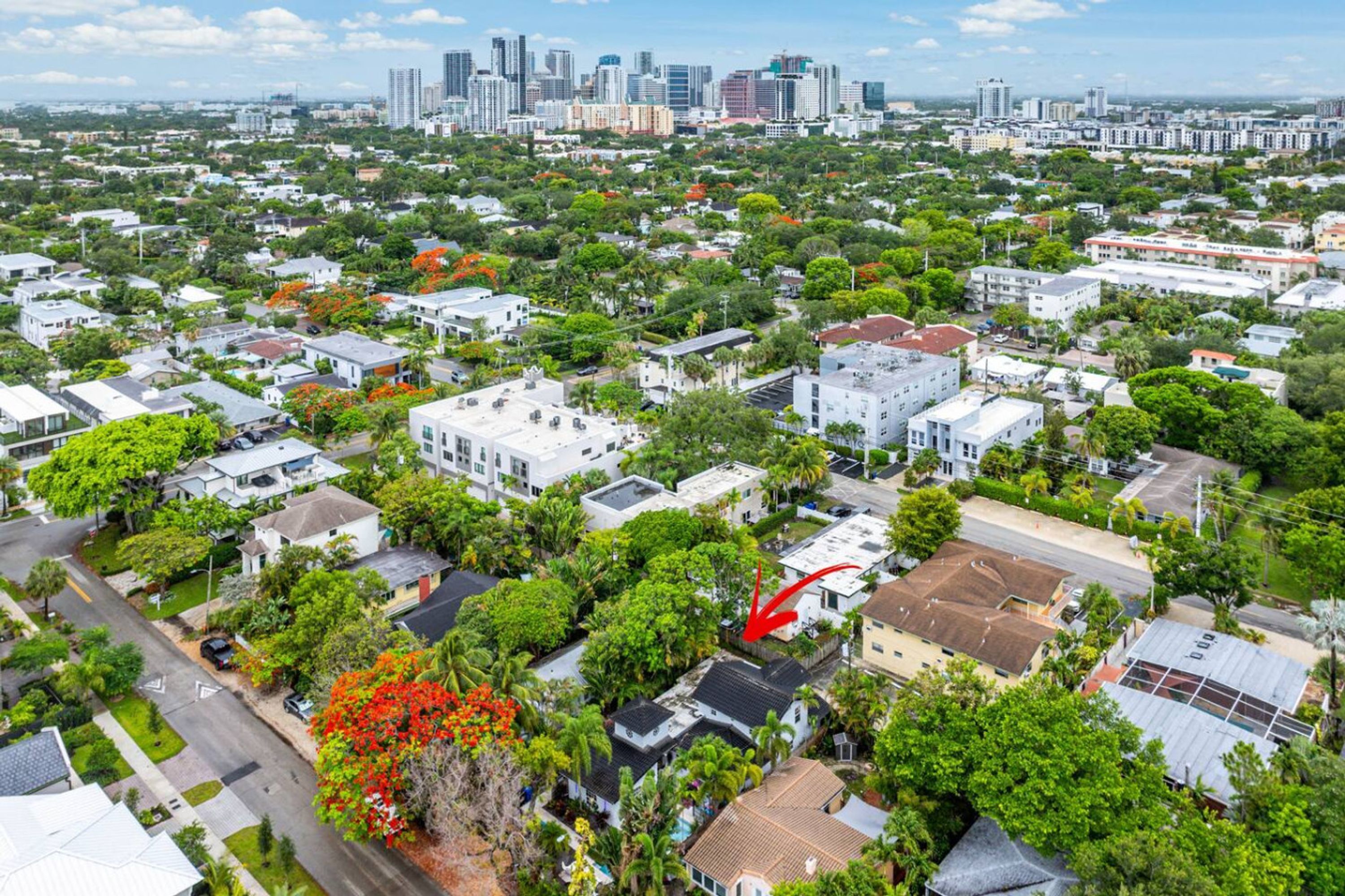 Une vue aérienne d’un quartier résidentiel, avec des maisons, des rues et, au loin, le profil urbain de la ville.