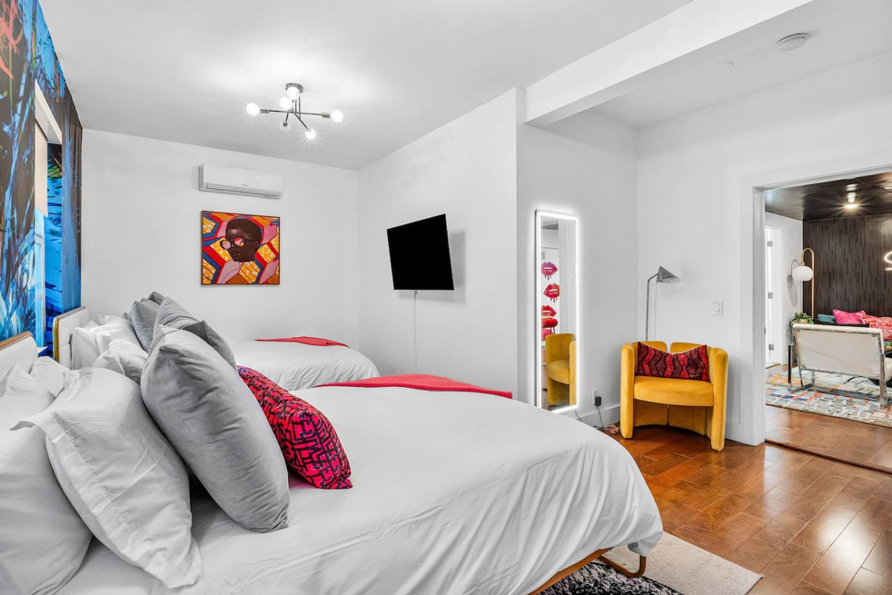 Una habitación de hotel moderna con una cama grande, un televisor de pantalla plana, un espejo y un pequeño rincón de descanso con una silla amarilla.