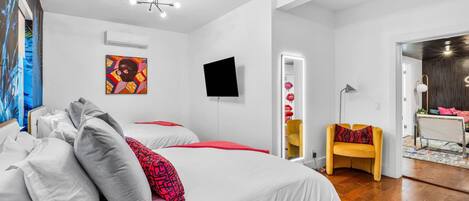 Una habitación de hotel moderna con una cama grande, un televisor de pantalla plana, un espejo y un pequeño rincón de descanso con una silla amarilla.