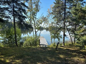 En träbrygga som sträcker sig ut i en stilla sjö, omgiven av tät skog.