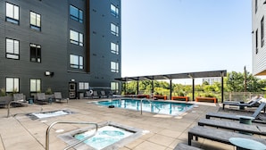 A rooftop pool area with lounge chairs, a hot tub, and a covered seating area.