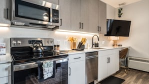 A modern kitchen with stainless steel appliances, a flat-screen TV, and a wooden floor.