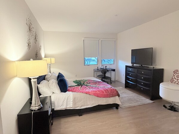 A bedroom with a bed, a desk, a dresser, a TV, and a chair.
