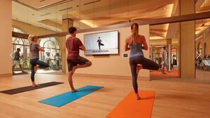 Un estudio de fitness con paredes de espejo, colchonetas de ejercicio y una pantalla grande que muestra una postura de yoga.