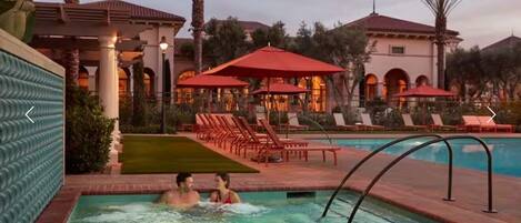 A pool area with hot tubs, lounge chairs, and umbrellas.