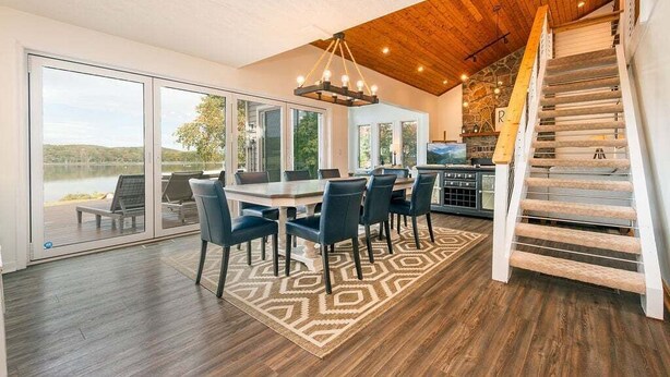A spacious dining area with a large table and chairs, a wooden staircase, and a view of the outdoors.